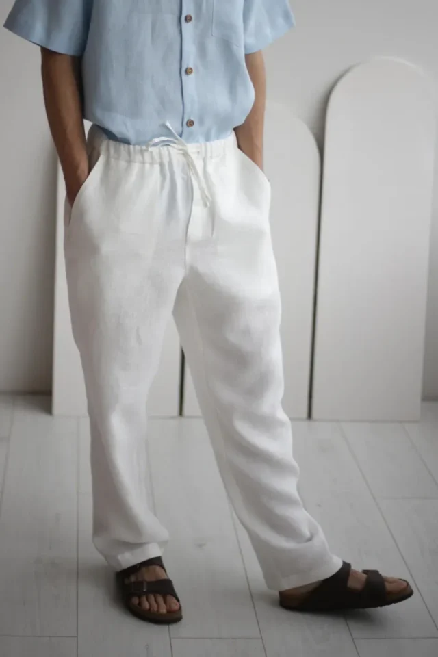 Side view of men`s white linen pants with pockets and adjustable waistband, demonstrating the relaxed yet sophisticated fit.